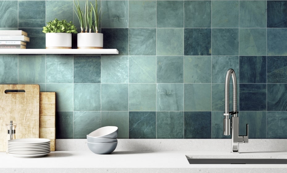 A sink setting with teal square shaped tiles as a splashback. There is a shelf with plants on and a chopping board to the the left. A sink with a tall tap is on the right.