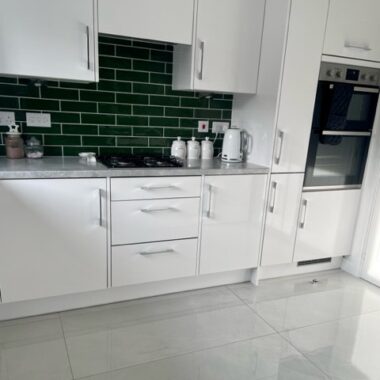 Close up of a kitchen counter with Scambio White Marble effect Kitchen tiles on the floor and metro dark green tiles on the wall
