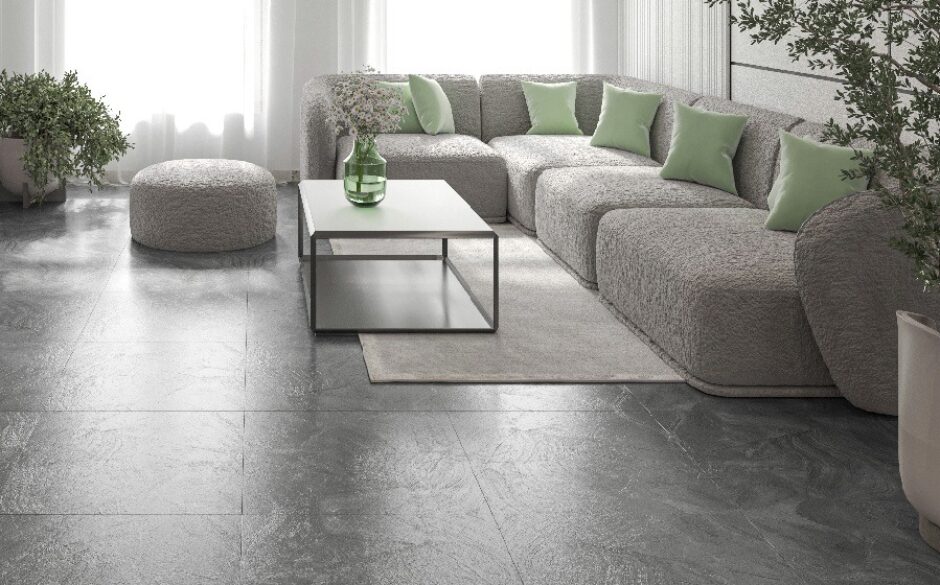A living room setting with an l shaped grey sofa accented with green scatter cushions. There is a coffee table on a large rug and black marble effect tiles on the floor.