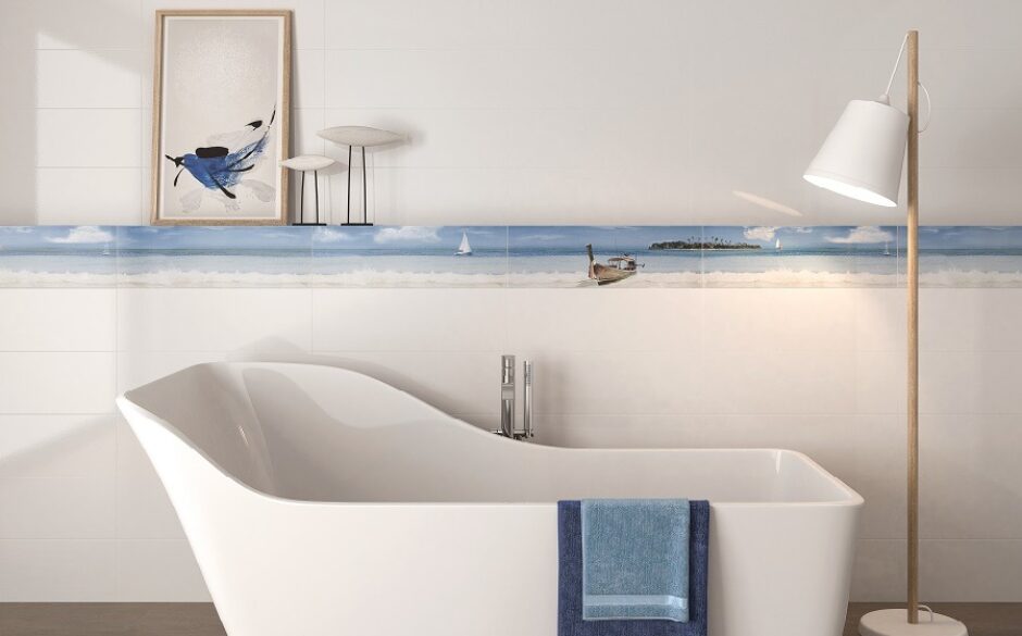 Artic White Ceramic Tiles in a bathroom setting. There is a slipper bath in the foreground with a shelf above it containing artwork of a bird. A wooden lamp with a white shade is on the right.