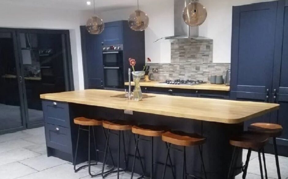 Kitchen with beautiful navy blue units. Wooden topped breakfast bar with metal stools and split face grey splashback tiles.