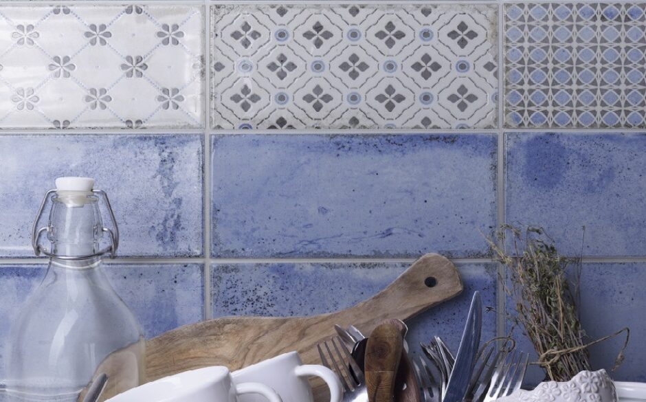 Close up of a kitchen wall with watercolour blue metro tiles and a row of patterned blue and white metro tiles. Chopping board and bottle.