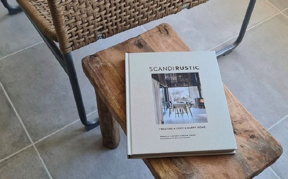A wicker chair with a wooden side table that has a Scandi design book on it.