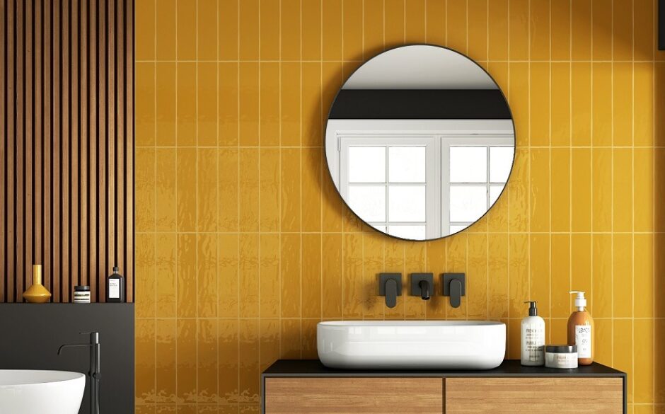 Vibrant mustard tiles in a bathroom setting. White sink under a circular mirror.