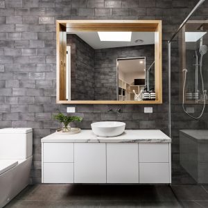 Vita Dark Grey Brick Tiles in a bathroom setting with white drawers and a rectangular wooden framed mirror.