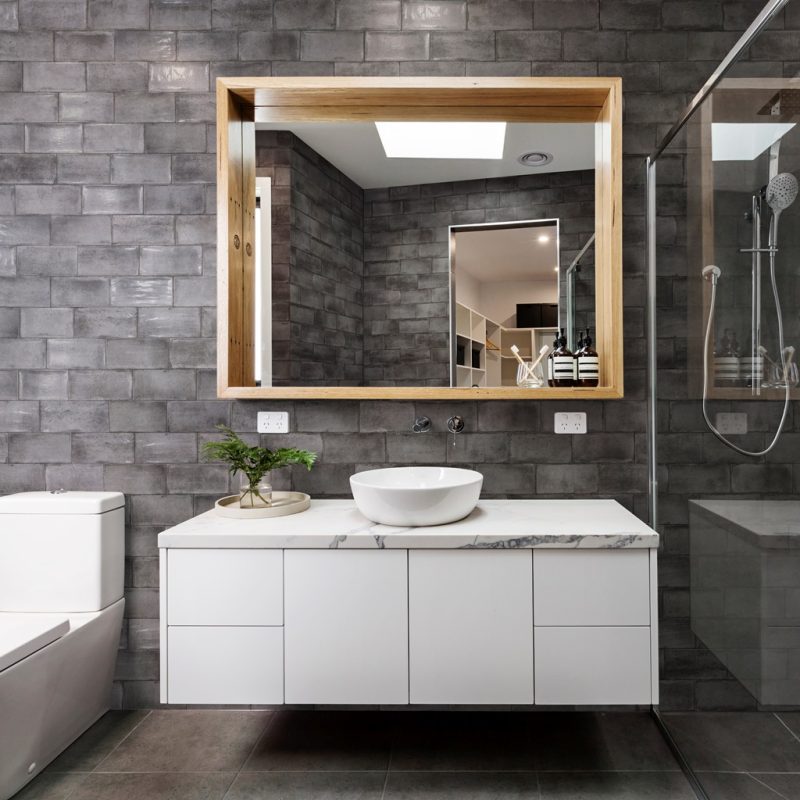 Vita Dark Grey Brick Tiles in a bathroom setting with white drawers and a rectangular wooden framed mirror.